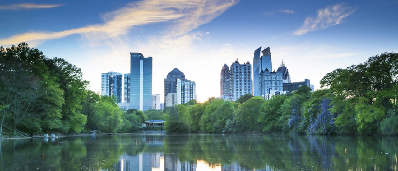 Atlanta skyline reflected in a calm lake surrounded by trees under a blue sky