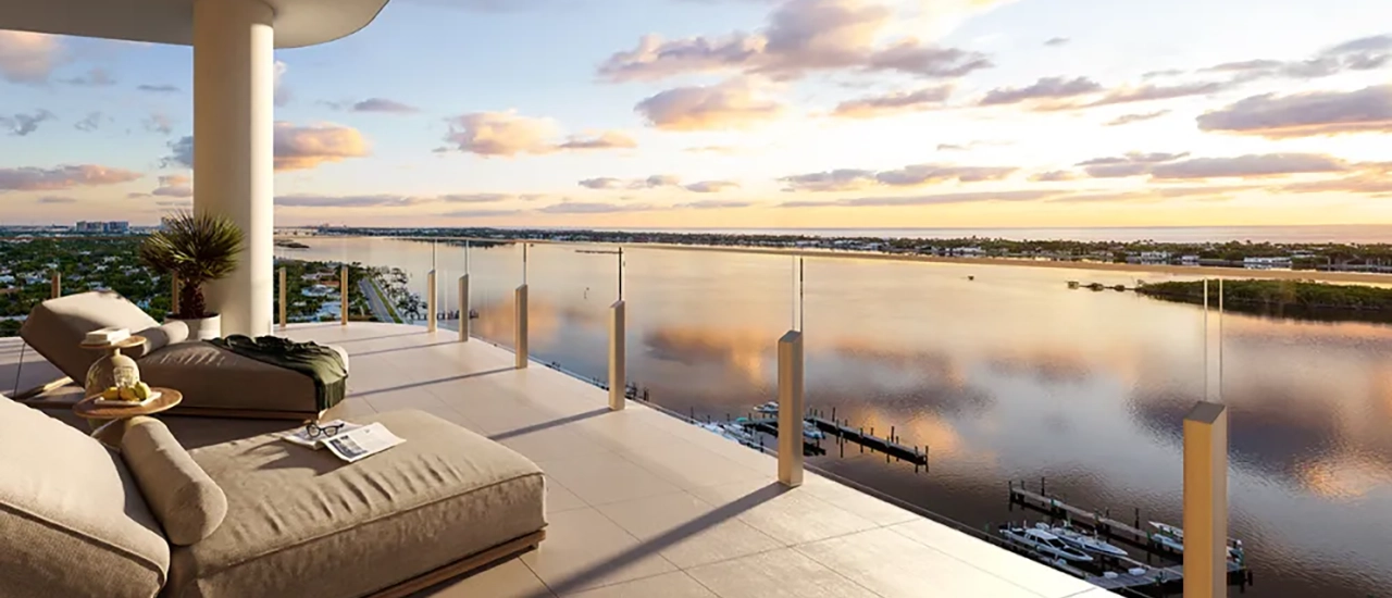 Penthouse terrace with lounge seating and glass railing overlooking a calm waterfront marina at sunset