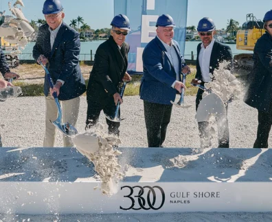 Executives in blue hard hats shovel concrete at a Kolt Naples groundbreaking ceremony.