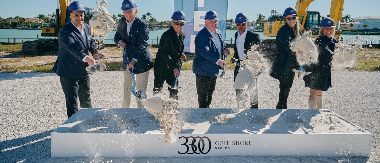 Executives in blue hard hats shovel concrete at a Kolt Naples groundbreaking ceremony.