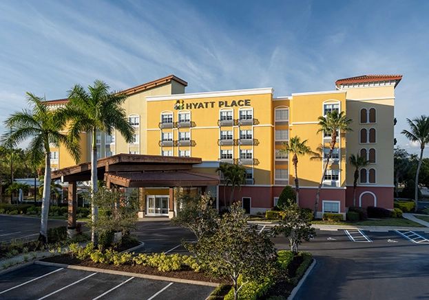 Yellow Hyatt Place hotel exterior with balconies, palm trees, and parking lot in front.