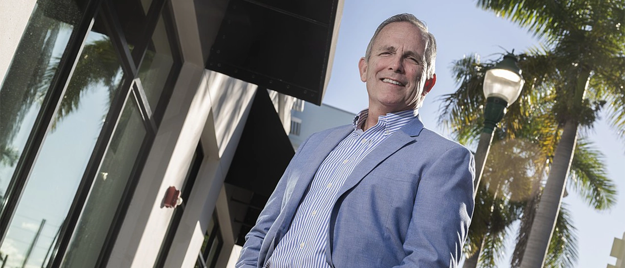 Man in blazer standing outside modern building with palm trees