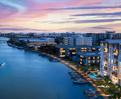 Aerial view of a coastal canal lined with modern apartment buildings at sunset; boats on the water.