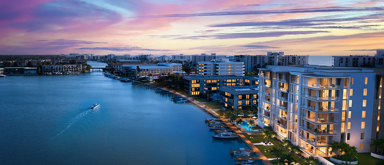 Aerial view of a coastal canal lined with modern apartment buildings at sunset; boats on the water.